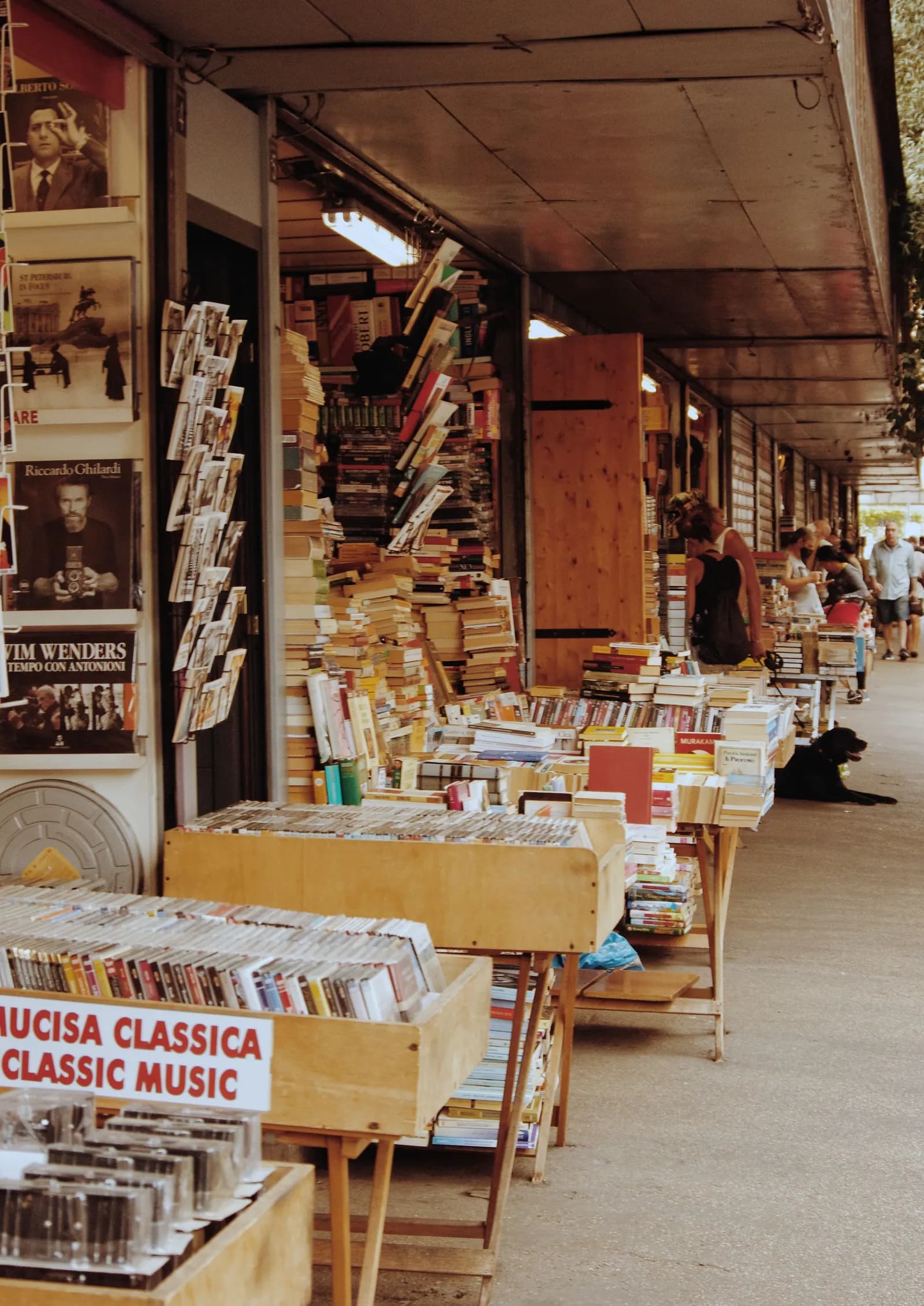 Un étal de bouquiniste en plein air avec des piles de livres et magazines italiens.