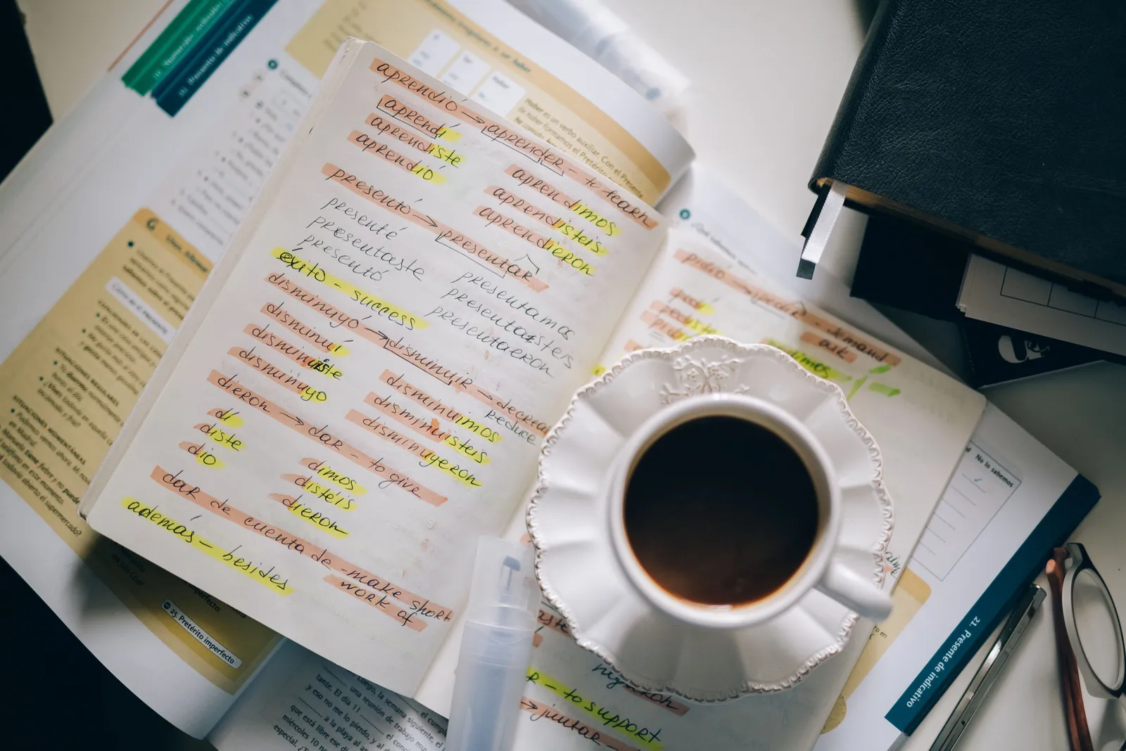 Un cahier avec des conjugaisons espagnoles annotées, à côté d'une tasse de café.